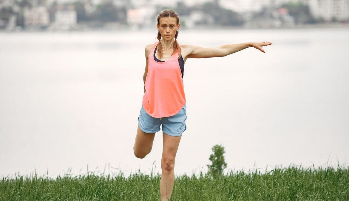Woman exercising and stretching by a lakeside in a peaceful outdoor setting.